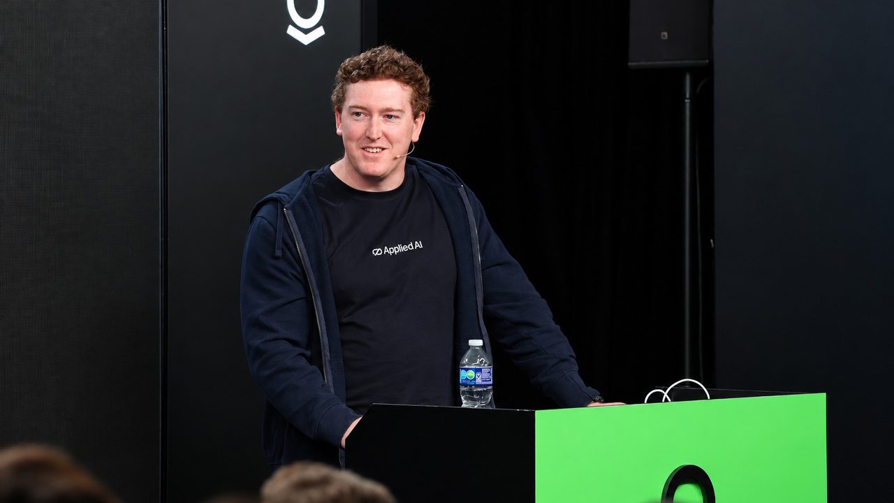 Phillip Kingston at the lectern on the Palantir DevCon 2024 stage in Palo Alto, California, in an AppliedAI T-shirt.